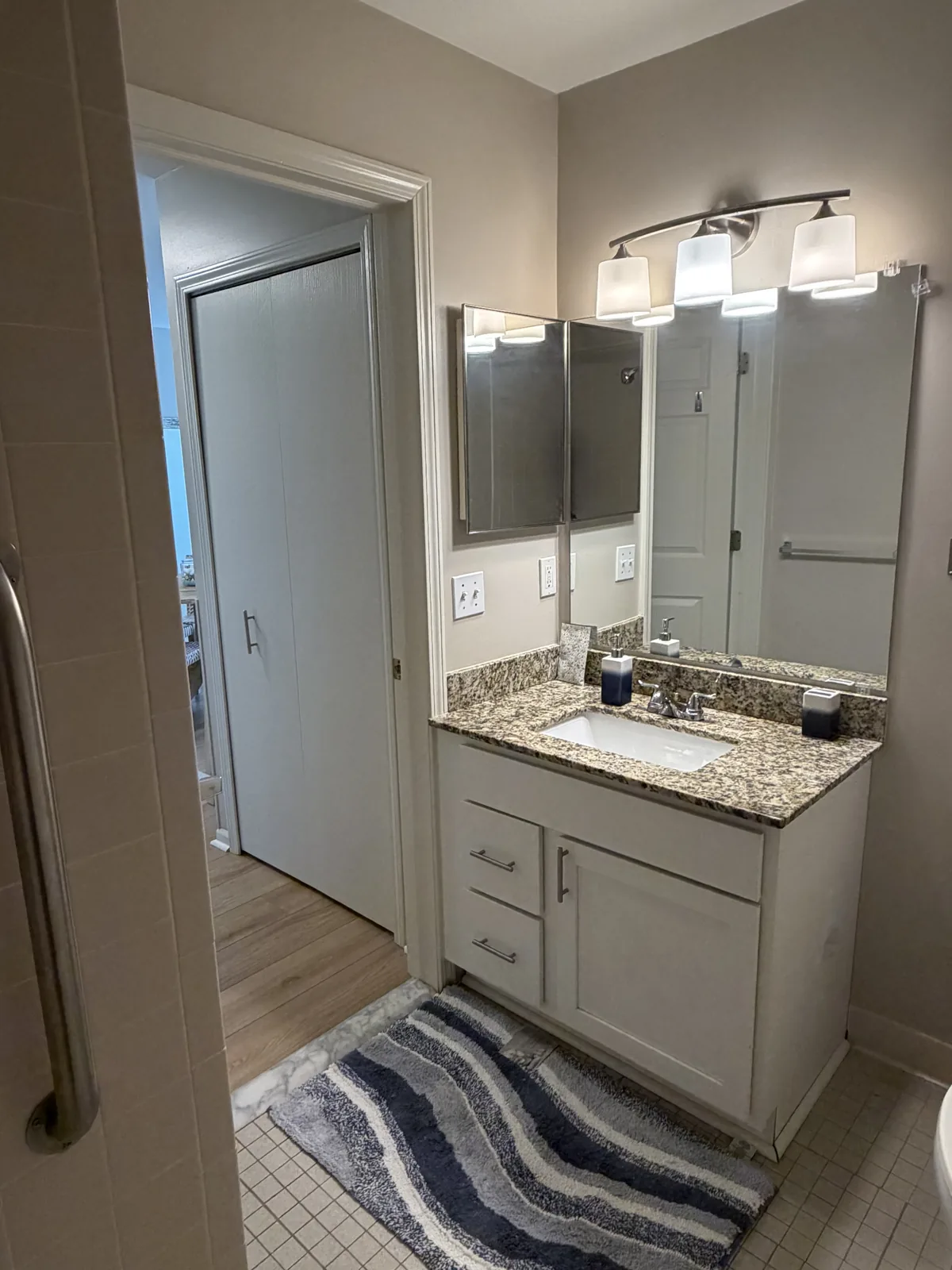 An apartment bathroom: granite vanity, mirror and lighting, with a step-in shower at Comfort Cove Senior Living in West Bloomfield, MI