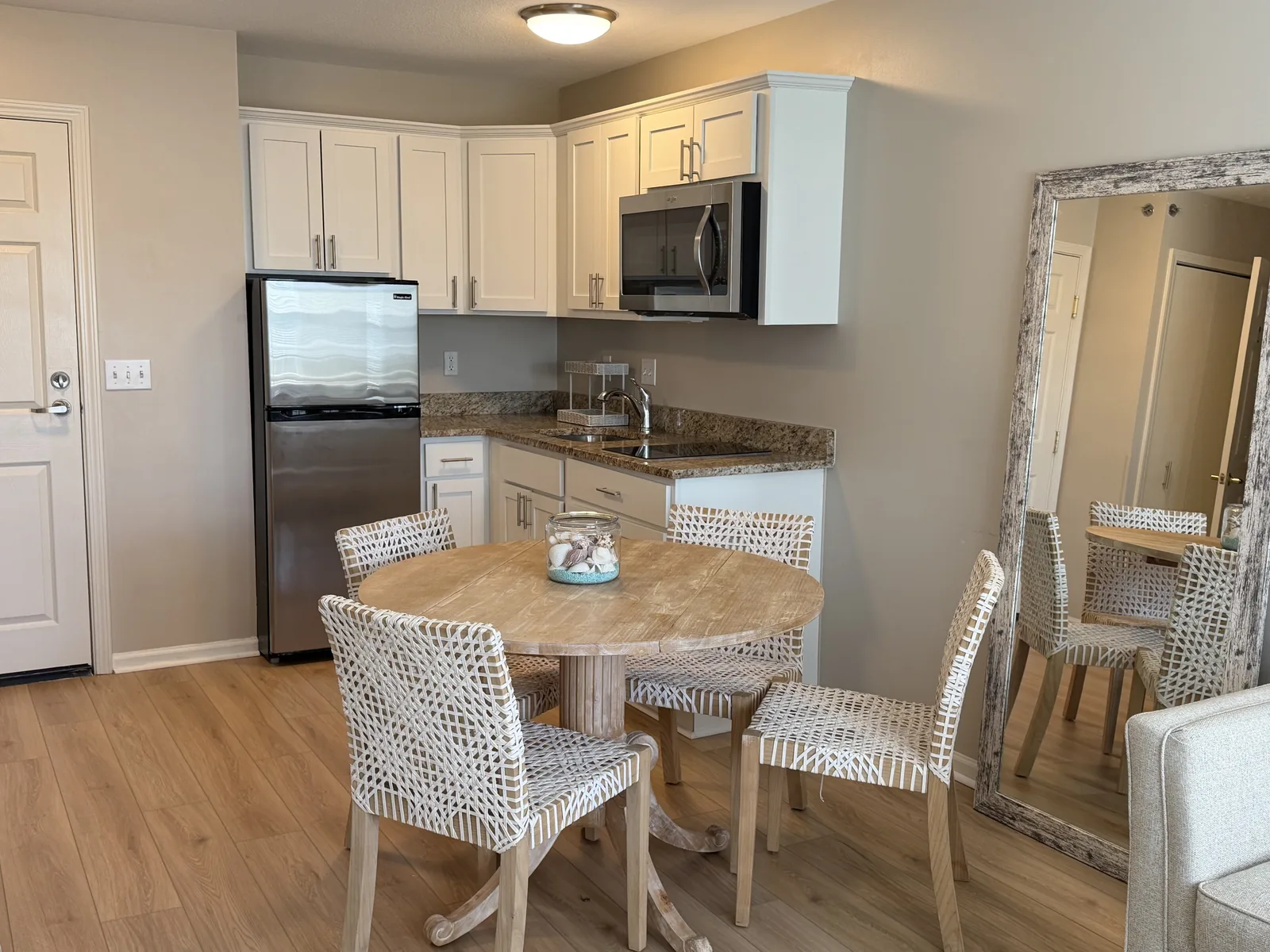 An apartment kitchenette: white cabinets, granite counter, stainless refrigerator and microwave, with a round dining table at Comfort Cove Senior Living in West Bloomfield, MI